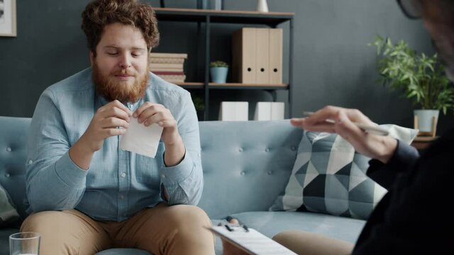 Nervous male patient is speaking to psychotherapist during appointment in office discussing problems expressing grief and sadness. People and emotions concept.