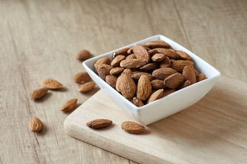 Tasty almond nuts in bowl on a wooden cutting board on wooden table, side view. Space for text