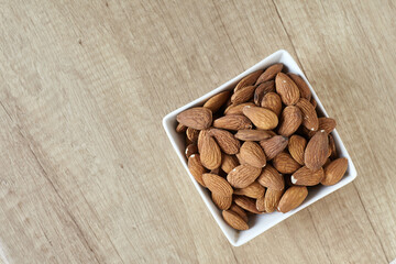 Tasty almond nuts in a bowl on a wooden table, top view. Space for text