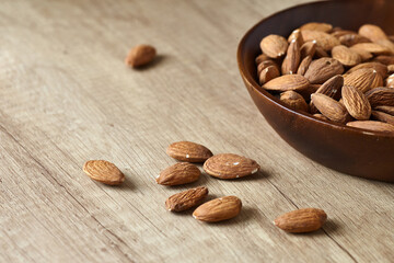 Tasty almond nuts in a wooden bowl on a wooden table, side view. Space for text