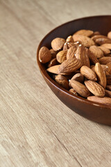 Tasty almond nuts in a wooden bowl on a wooden table, side view. Space for text