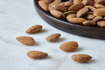 Tasty almond nuts on a wooden plate on a marble table, side view. Space for text