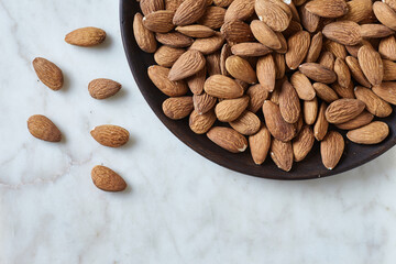Tasty almond nuts on a wooden plate on a marble table, top view. Space for text