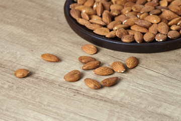 Tasty almond nuts on a wooden plate on a wooden table, side view. Space for text