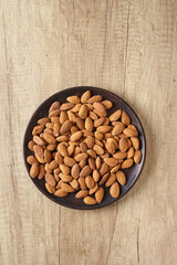 Tasty almond nuts on a wooden plate on a wooden table, top view. Space for text