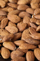 Tasty almond nuts on a wooden plate on a wooden table, top view. Space for text