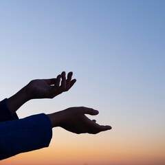 hands raised up against the background of the sunset dark sky