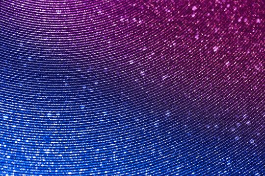 Wavy shimmering blue background. Texture with grain and purple sequins close-up. Gradient two-color image