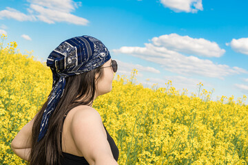 A girl in sunglasses and a bandana looks at the sky against the background of a blooming field