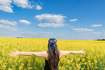 A girl with open arms stands against the background of a blooming rapeseed field