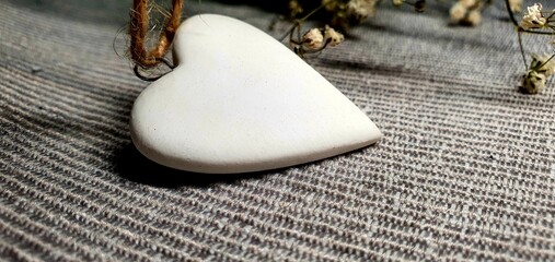 White pendant in the shape of a heart. White heart decoration. Love background. Delicate composition with a heart and flowers.