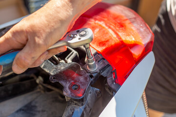 Motorcycle repair and maintenance. The man unscrews the fasteners with a socket wrench.