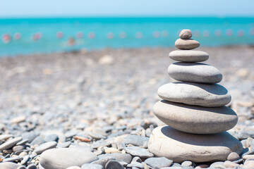 Fototapeta na wymiar Round stones are stacked on top of each other in a pyramid on the seashore on a sunny day. Balance concept. Copy space.