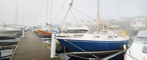 Elegant and modern sailboats moored to a pier in a yacht marina. Thick white fog. Stavanger,...