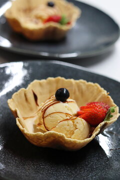 Scoop of homemade walnut ice cream, accompanied with blueberry and strawberry and decorated with caramel syrup, in a biscuit basket. Vertical image.