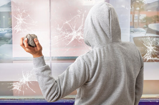 Rear view of a man holding a stone to throw it against a glass and break a window.