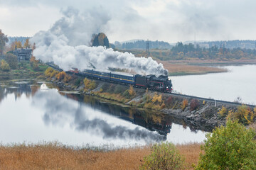 Fototapeta na wymiar Retro steam train moves along the lake at autumn cloudy time. Karelia.