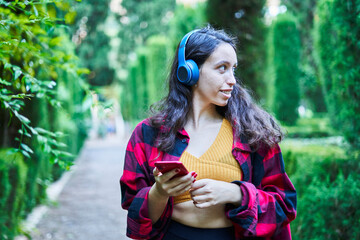 brunette girl walking through the park gardens listening to music with headphones