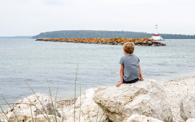 Fototapeta na wymiar A young kid is sitting on a rock to enjoy a quiet day