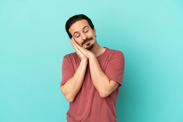 Young caucasian man isolated on blue background making sleep gesture in dorable expression