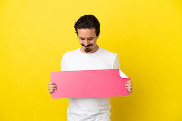 Young caucasian man isolated on yellow background holding an empty placard