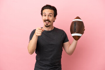 Young caucasian man playing rugby isolated on pink background surprised and pointing front