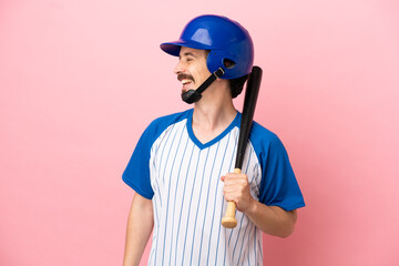 Young caucasian man playing baseball isolated on pink background looking side
