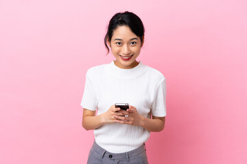 Young Vietnamese woman isolated on pink background sending a message with the mobile