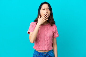 Young Vietnamese woman isolated on blue background yawning and covering wide open mouth with hand