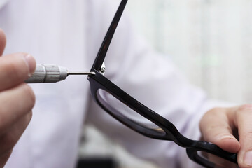 Close-up. The hands of a master repairing glasses: he screws a bolt with a screwdriver. Optics salon concept