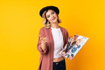 Young artist girl holding a palette isolated on yellow background handshaking after good deal