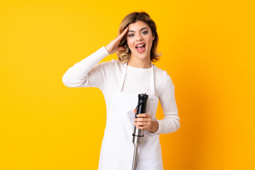 Girl using hand blender isolated on yellow background with surprise expression