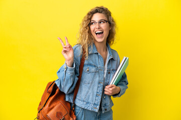 Young student caucasian woman isolated on yellow background smiling and showing victory sign