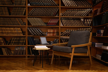 Cozy home library interior with comfortable armchair, laptop and collection of vintage books on shelves