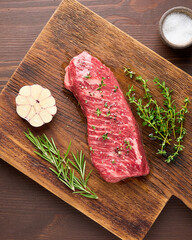 Raw tender and marbled striploin steak with salt, garlic clove and spices rosemary and thyme on wooden board. Uncooked sirloin beef. Preparation for cooking. Vertical, overhead