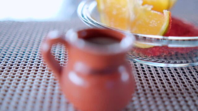 Clay cup and plate of orange slices on gray table mat