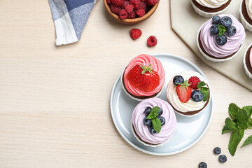 Sweet cupcakes with fresh berries on light wooden table, flat lay. Space for text
