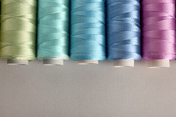 Different colorful sewing threads on light grey background, flat lay. Space for text
