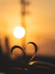 An open book with heart-shaped pages against a beautiful sunset