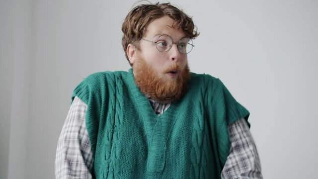 Slow motion portrait of chubby young man making funny grimaces and looking at camera against white background. Crazy people and behavior concept.