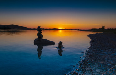 sunset on the river. Sunset on the background of the cairn. Balance of stones on the background of sunset by the water.