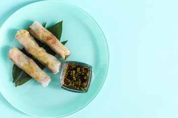 Spring rolls of seafood and vegetables with a decor of green leaves on a light background.	