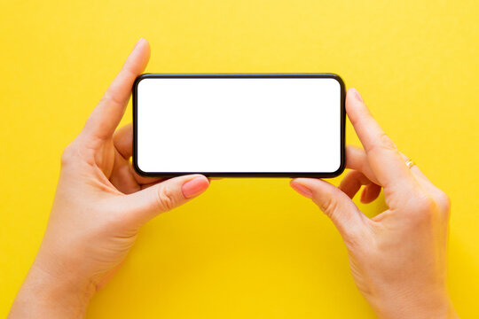 Mobile phone with empty white screen held in hands horizontally on yellow background