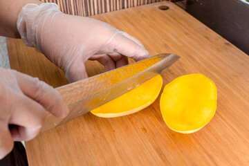 Slicing a ripe mango with a kitchen knife while wearing plastic gloves. Ingredient for California...