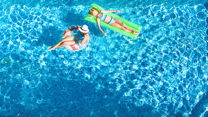 Children in swimming pool aerial drone view from above, happy kids swim on inflatable ring donut and mattress, active girls have fun in water on family vacation on holiday resort
