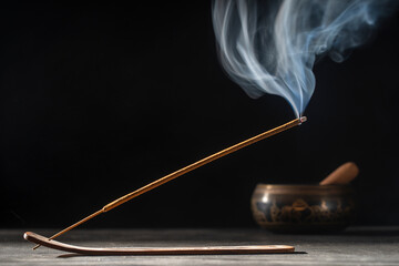 Asian incense stick in stick holder burning with smoke on black background