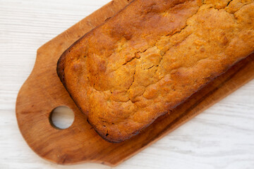 Homemade Pumpkin Loaf Bread on a rustic wooden board on a white wooden surface, top view. Flat lay, overhead, from above.