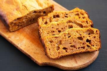 Homemade Pumpkin Loaf Bread on a rustic wooden board on a black surface, low angle view.