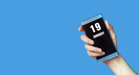 january 19. 19th day of the month, calendar date.Woman's hand holds mobile phone with blank screen on blue isolated background.Winter month, day of the year concept