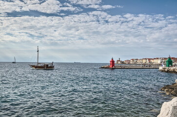 View of the red and green lighthouses on a pier,  boat and the architecture of  the city on the horizon, Piran, Slovenia.